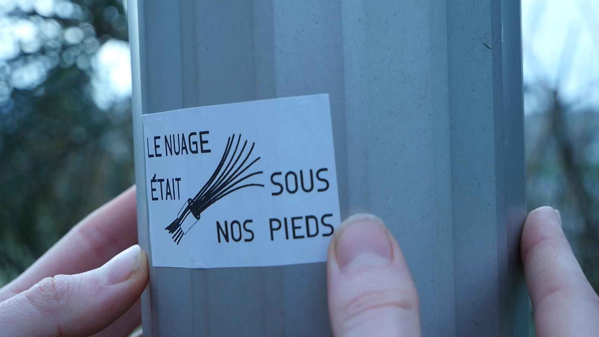Sticker Le nuage était sous nos pieds on a street pole. Photo taken during the Le Nuage était sous nos pieds festival walk on November 9, 2024. Sticker made during the festival's workshop organized by the transfeminist hackerspace Fluidspace in Marseille.